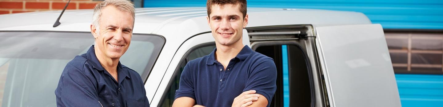 A father and son plumbing team stand next to their van with arms crossed 