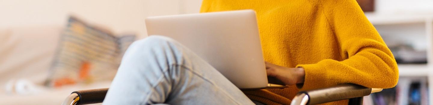 An image of a laptop on the lap of a person wearing a yellow jumper