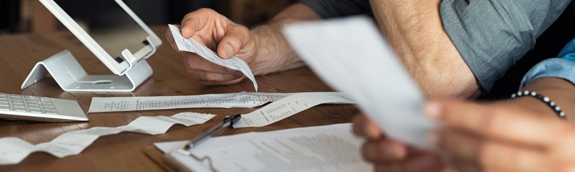 Two people sit looking at receipts on a table, only their hands are visible 