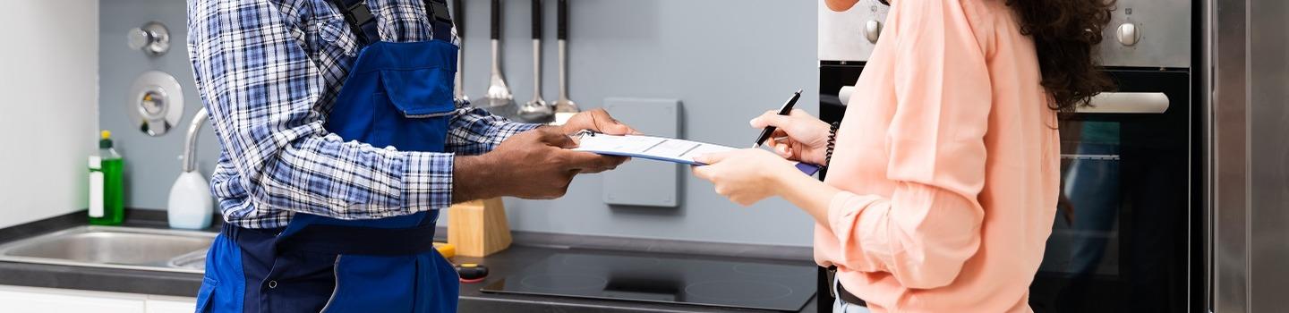 A close up shot of two pairs of hands. Male hands dressed in workman's attire holds out a clipboard while a woman's hands dressed in a casual jumper signs the bottom of the clipboard. 