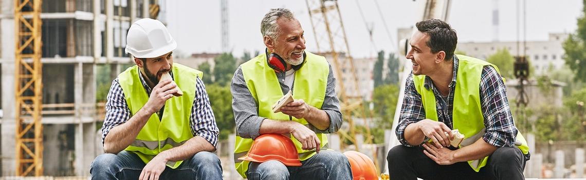 Builders sit on a wall eating sandwiches